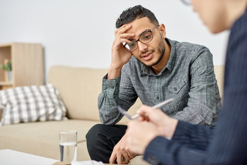 man sitting down and talking with hands on his head