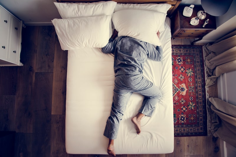 man lying in bed with pillows over his head