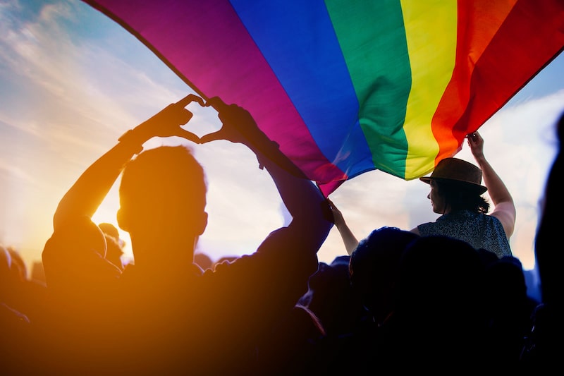 people in the sunset with lgbtq flag flying in the wind