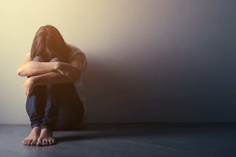 woman on the ground covering her face with her head on her knees