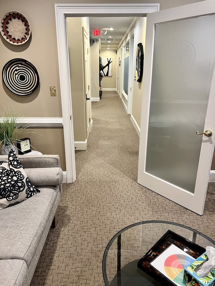 Looking down the hall from an office containing a light gray couch and coffee table